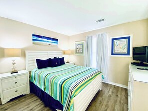 A bedroom with a bed, two bedside tables, a television, and artwork on the walls.