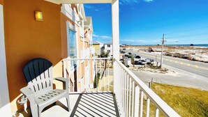 Un balcón con una silla blanca, vista a una playa y una carretera con vehículos.