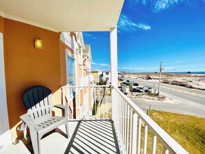 A balcony with a white chair, a view of a beach, and a road with vehicles. - Grand Beach 315 - Beach View - Great location in the heart of Gulf Shores! (Gulf Shores)