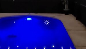 A swimming pool with a blue illuminated surface, surrounded by a dark area with string lights.