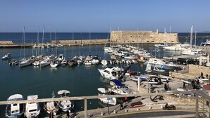 Un puerto deportivo con varias embarcaciones amarradas, una fortaleza de piedra al fondo y un cielo azul despejado.
