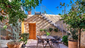 Un patio con una mesa y sillas, rodeado de plantas en macetas y una escalera de piedra.