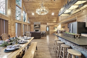 A spacious cabin interior with a long dining table set for a meal, a bar area with stools, and a fireplace.