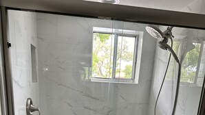 Eine begegnete Dusche mit Duschbrause, einem kleinen Fenster und einer Haltestange.