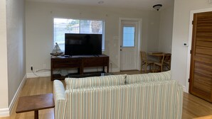Ein Wohnzimmer mit Sofa, Fernseher, Deckenventilator und einem Essbereich mit Stühlen.