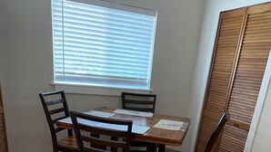 Ein Essbereich mit Holztisch und -stühlen, einem Fenster mit Jalousien sowie einem Holzboden.