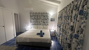 Une chambre à coucher avec un lit, des rideaux, une table de chevet, une lampe et un appareil de climatisation.