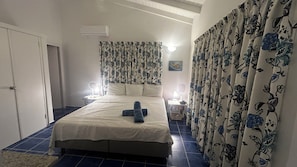 A bedroom with a bed, curtains, a bedside table, a lamp, and an air conditioning unit. - Marazul Dive Resort. 3 Bedroom Seafront house. Dive, Snorkel, amazing sunsets (Sabana Westpunt)