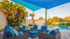Eine Außenpatio mit Korbmöbeln, einem Pool und einem blauen Sonnensegel.