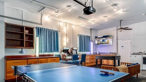 Ein Zimmer mit einer Tischtennisplatte, Holzschränken, einer Küchenzeile und einem Deckenventilator.