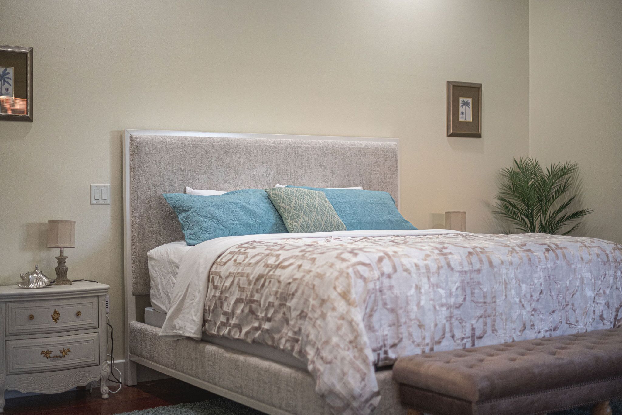 A neatly made bed with a patterned bedspread, a bedside table with a lamp, and a small plant beside the bed.