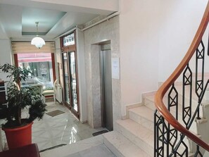 Eine Hotelhalle mit Marmorboden, einer Treppe mit schwarzen Metallgeländern und einem Blumentopf.