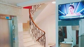 A hotel lobby with a marble staircase, a television mounted on the wall, and a reception desk. - Daylight Rezidans (Istanbul)