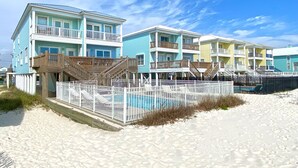Un hotel frente a la playa con varios balcones, piscina y una zona de playa arenosa.