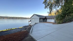 Uma casa com garagem e rampa de acesso coberta, com vista para um lago e céu claro.