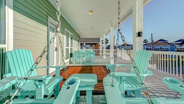 A porch with turquoise Adirondack chairs and a swing set.