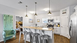 A modern kitchen with a central island, bar stools, white cabinets, stainless steel appliances, and a green door.