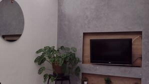 Un salon moderne avec un téléviseur à écran plat fixé à un mur gris, un miroir rond et une plante en pot posée sur une petite table.