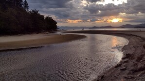 Une plage au rivage incurvé, avec une eau calme et une zone boisée en arrière-plan.
