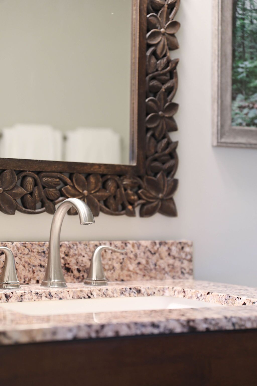 A bathroom with a granite countertop, a silver faucet, and a decorative mirror frame with a floral design.