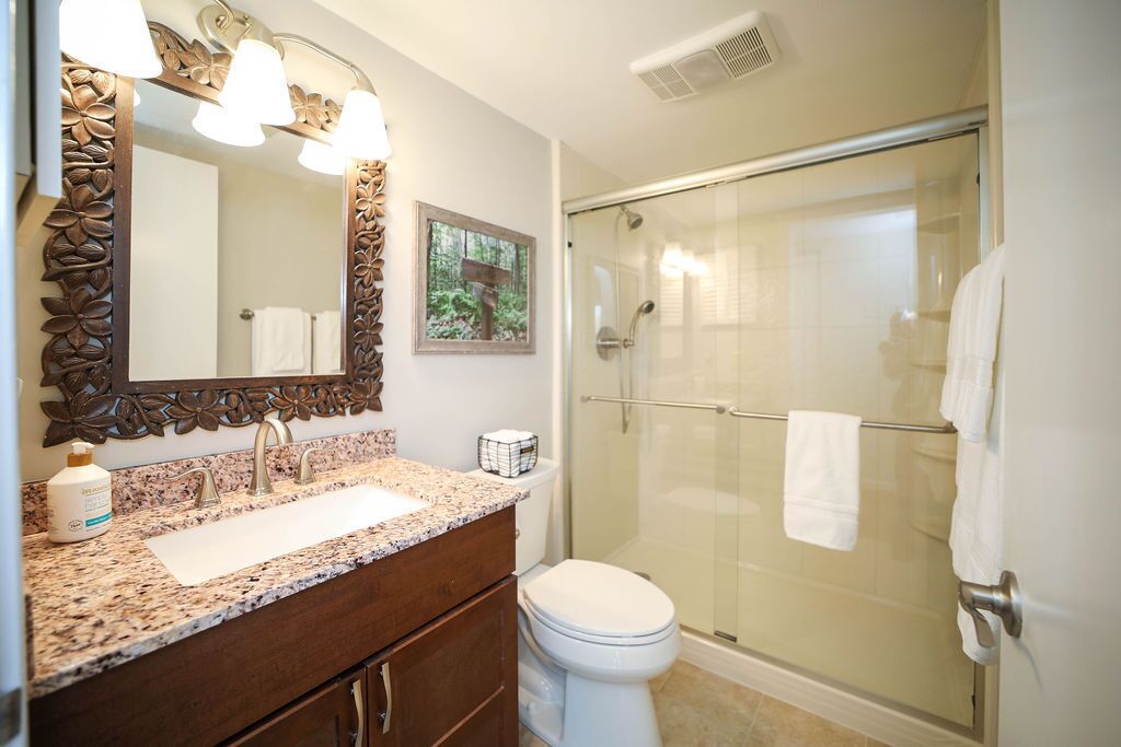 A bathroom with a granite countertop, a large mirror, a shower with glass doors, and a toilet.