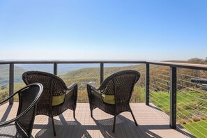 Un balcon avec des fauteuils en osier et une vue sur une vallée.