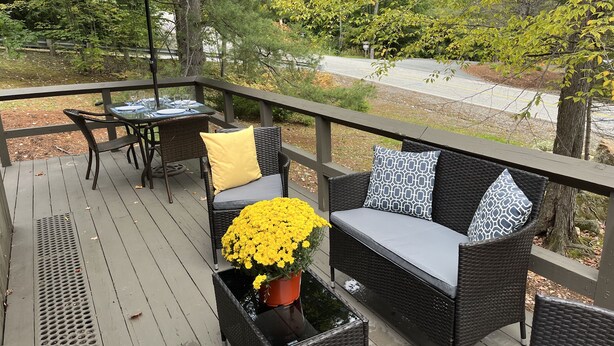 Une terrasse extérieure couverte, aménagée avec des meubles en osier, une table dressée pour le repas et un pot de fleurs orné de fleurs jaunes.