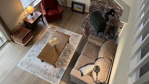 Un salon avec un canapé, un fauteuil rouge, une table basse, une cheminée et une lampe.