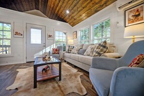 A cozy living room with a wooden ceiling, a sofa with patterned cushions, a glass coffee table, and a large window. - 27 Private Acres / Pet Friendly/ Fishing Pond (Broken Bow)