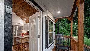 Une terrasse en bois avec une chaise, un coin cuisine équipé d’un réfrigérateur et une porte donnant sur un espace extérieur.
