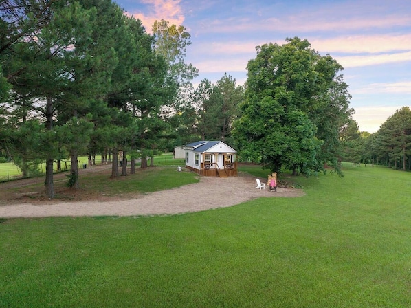 A small cabin with a porch, surrounded by a grassy field and trees.