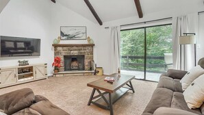 Ein Wohnzimmer mit Kamin aus Stein, einem großen Fenster mit Blick auf Grünflächen, einer Couch und einem Couchtisch.