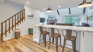 Eine moderne Küche mit Kochinsel, Barhocker, Pendelleuchten und Kamin.