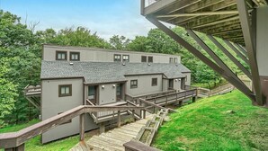 Ein zweistöckiges Gebäude mit grauer Fassade und geneigtem Dach, verbunden durch Holztreppen und Geländer.