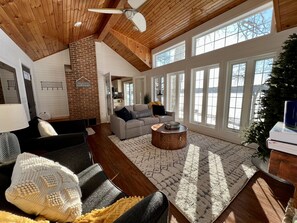 A spacious living room with a high ceiling, large windows, and a cozy fireplace.