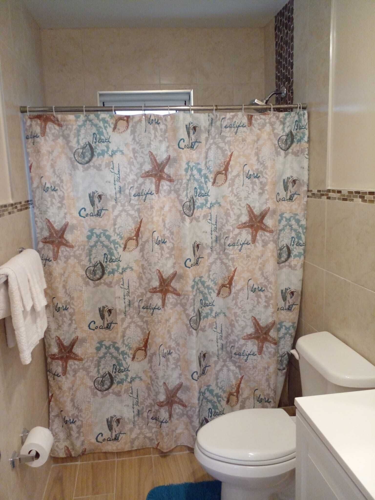 A bathroom with a shower curtain featuring a beach and sea life pattern, a toilet, and a towel rack.