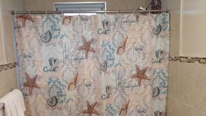 Une salle de bain avec un rideau de douche orné d’un motif représentant une plage et des animaux marins, des toilettes et un porte-serviettes.
