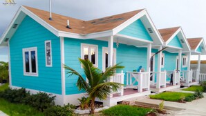 Une rangée de maisons aux couleurs turquoise et blanche, chacune dotée d’un porche et d’un palmier devant.