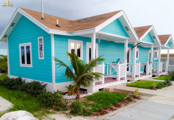 Une rangée de maisons aux couleurs turquoise et blanche, chacune dotée d’un porche et d’un palmier devant.