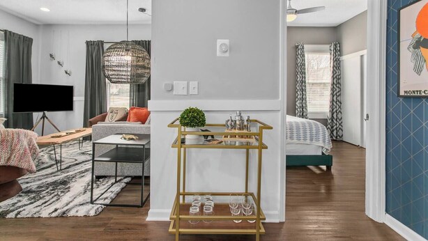 Un salon moderne avec un canapé, une table basse et un téléviseur. Il y a également un coin repas avec une table et des chaises. La pièce est dotée d’une grande fenêtre avec des rideaux.