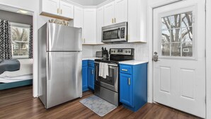 Une cuisine compacte avec des meubles blancs, un réfrigérateur en acier inoxydable, un four à micro-ondes, une cuisinière et des touches de couleur bleue.