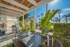 An outdoor patio with a table and chairs, surrounded by tropical plants and palm trees. - 2 Bedroom Oceanfront w/ Patio on the Boardwalk (Newport Beach)