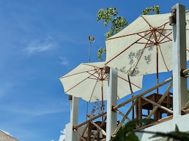Una estructura con varios paraguas blancos sujetos a una armazón de madera, con un cielo azul despejado de fondo.