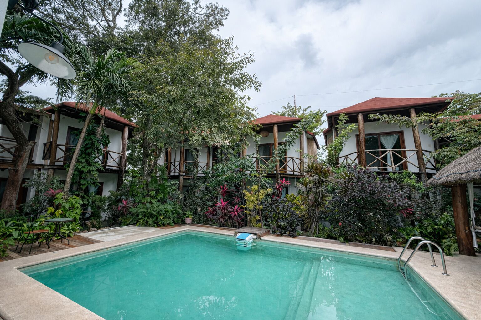 Una piscina rodeada de exuberante vegetación y edificios de madera con tejados rojos.