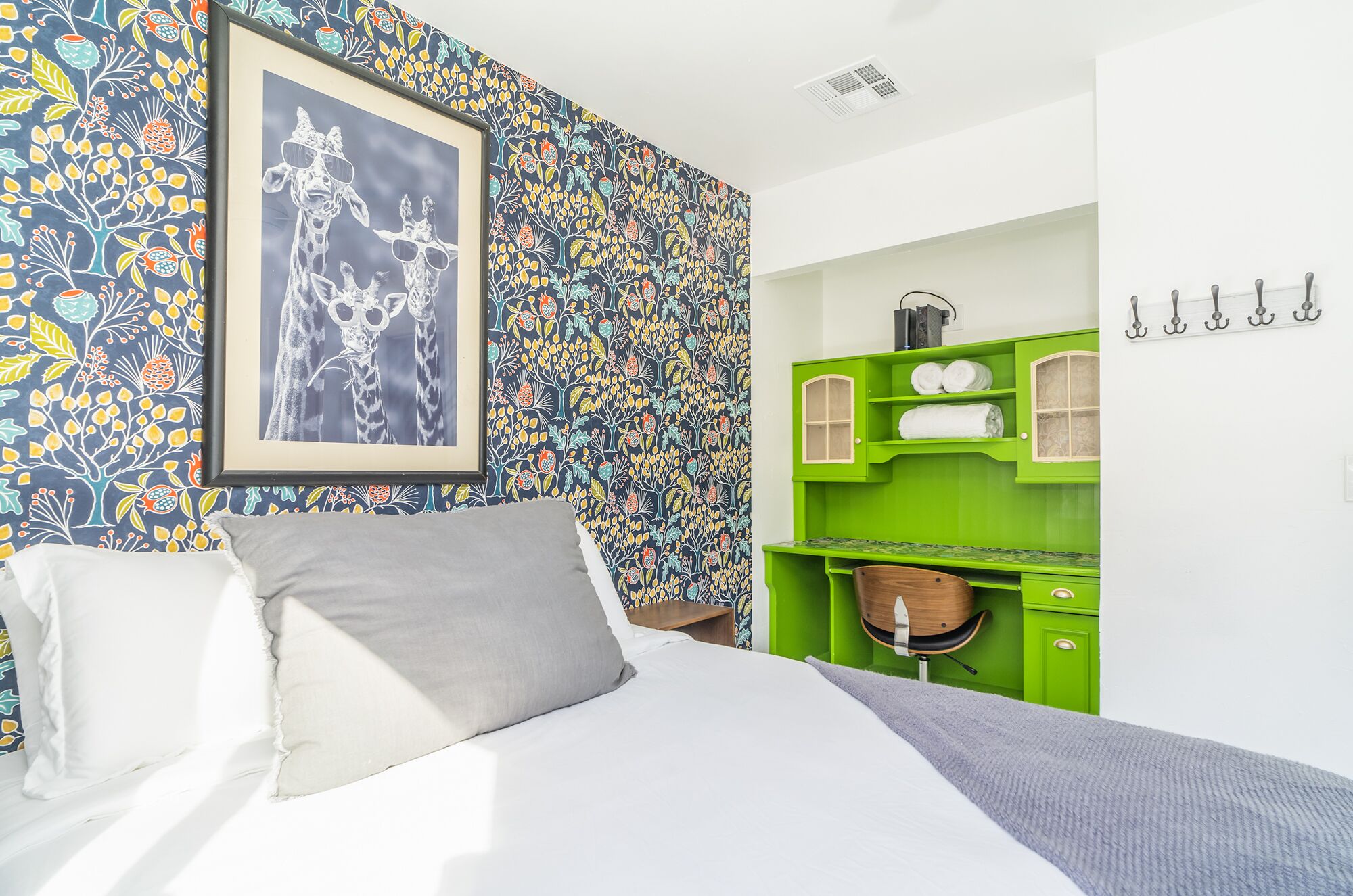 Un dormitorio con cama, una kitchenette verde y un llamativo papel tapiz floral.