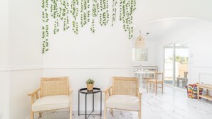 Una habitación luminosa con dos sillones de mimbre, una mesita con una planta y una instalación colgante de plantas.