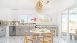 Una cocina moderna con armarios blancos, un comedor con una mesa redonda y sillas de madera, y amplias ventanas con vistas al exterior.