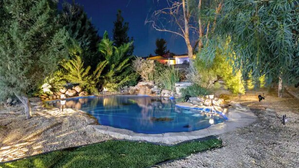Una piscina rodeada de árboles y rocas, con vista a una casa al fondo.