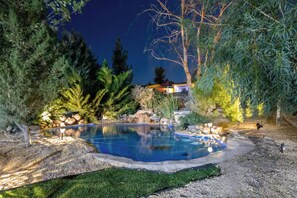 A swimming pool surrounded by trees and rocks, with a view of a house in the background.