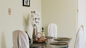 Un coin repas avec une table en marbre, deux chaises recouvertes de tissu, un vase de fleurs blanches et un tableau encadré au mur.